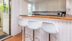 Een keuken met witte houten kastjes, een houten aanrecht en drie witte barstoelen.