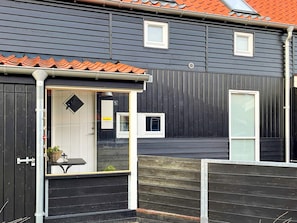 A building with a dark facade, a tiled roof, and a small outdoor seating area with a table and chairs. - 4 Star Holiday Home in Juelsminde (Juelsminde)
