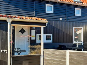 A wooden deck with a glass enclosure, a small table, and chairs. - 4 Star Holiday Home in Juelsminde (Juelsminde)