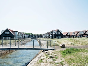 A row of modern houses with a river in the foreground and a bridge connecting them. - 4 Star Holiday Home in Juelsminde (Juelsminde)