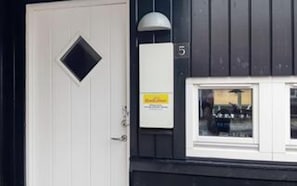 A building with a white door, a window with a view of parked cars, and a sign on the wall. - 4 Star Holiday Home in Juelsminde (Juelsminde)