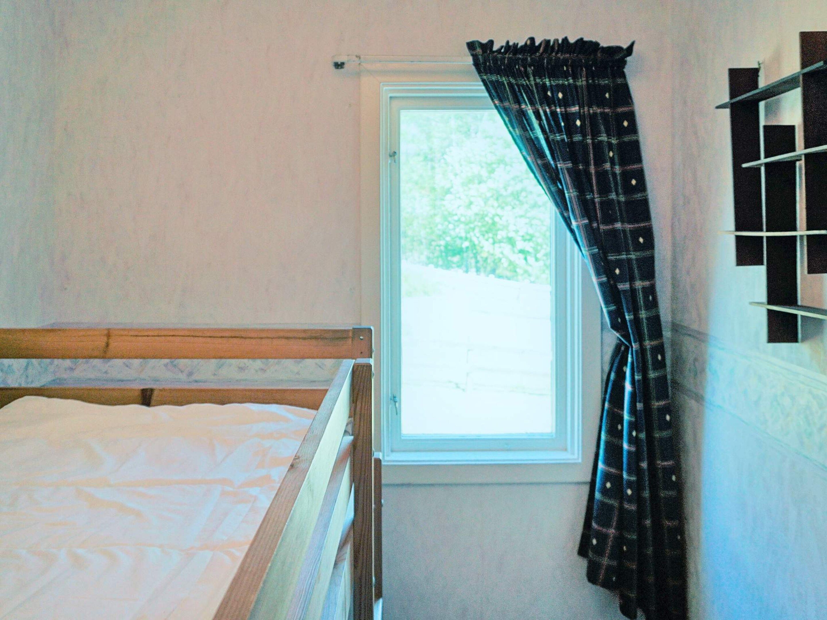 Uma cama de solteiro num quarto com janela e cortina.