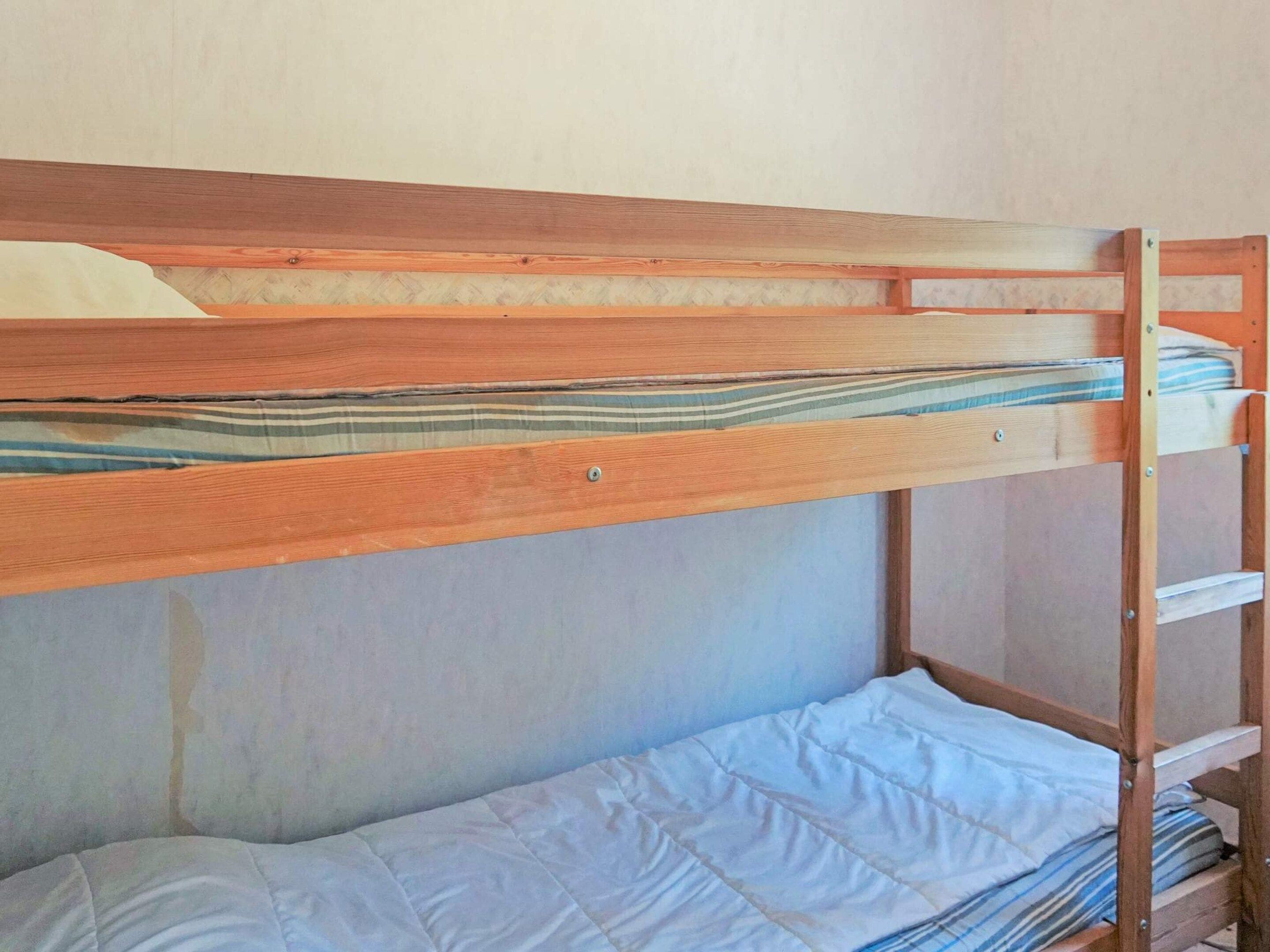 A bunk bed with a wooden frame and a lower bed with a white mattress.