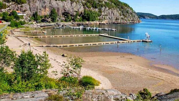 Una zona costera con acantilados rocosos, una playa de arena y un puerto deportivo con barcos.