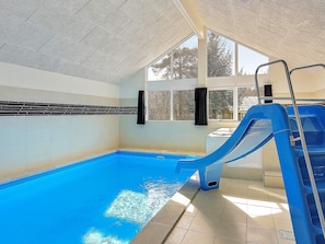 An indoor swimming pool with a blue slide, tiled walls, and large windows.