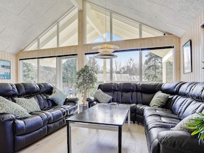 A spacious living room with leather sofas, a glass coffee table, and large windows offering a view of the outdoors.