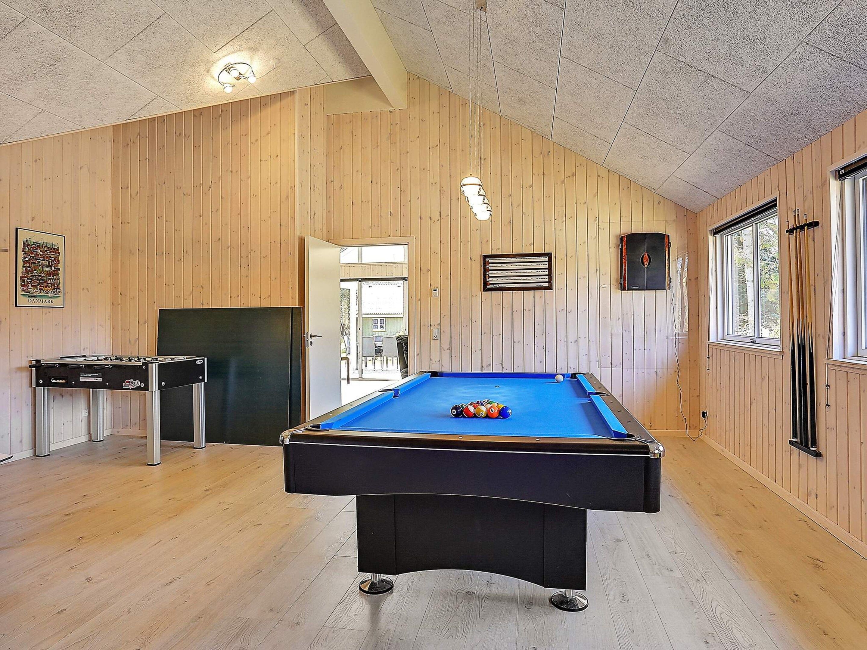 A pool table in a room with wooden walls and a ceiling with a geometric pattern.