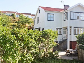 A two-story building with a red-tiled roof, a visible staircase, and a patio area with a table and chairs. - Holiday Home in Dyrön (Roennaeng)