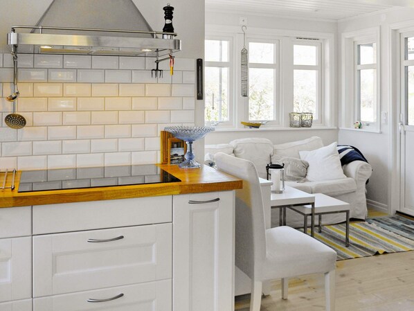 A modern kitchen with white cabinetry, a wooden countertop, and a hanging light fixture. - Holiday Home in Dyrön (Roennaeng)