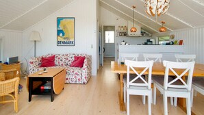 A cozy interior with a sofa, dining table, chairs, a lamp, and a kitchen area.