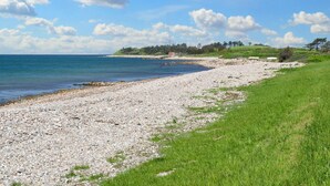 A pebbly beach with a grassy area and a clear sky.