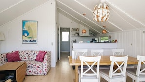 A cozy interior with a wooden dining table, white chairs, a floral sofa, and a kitchen area.
