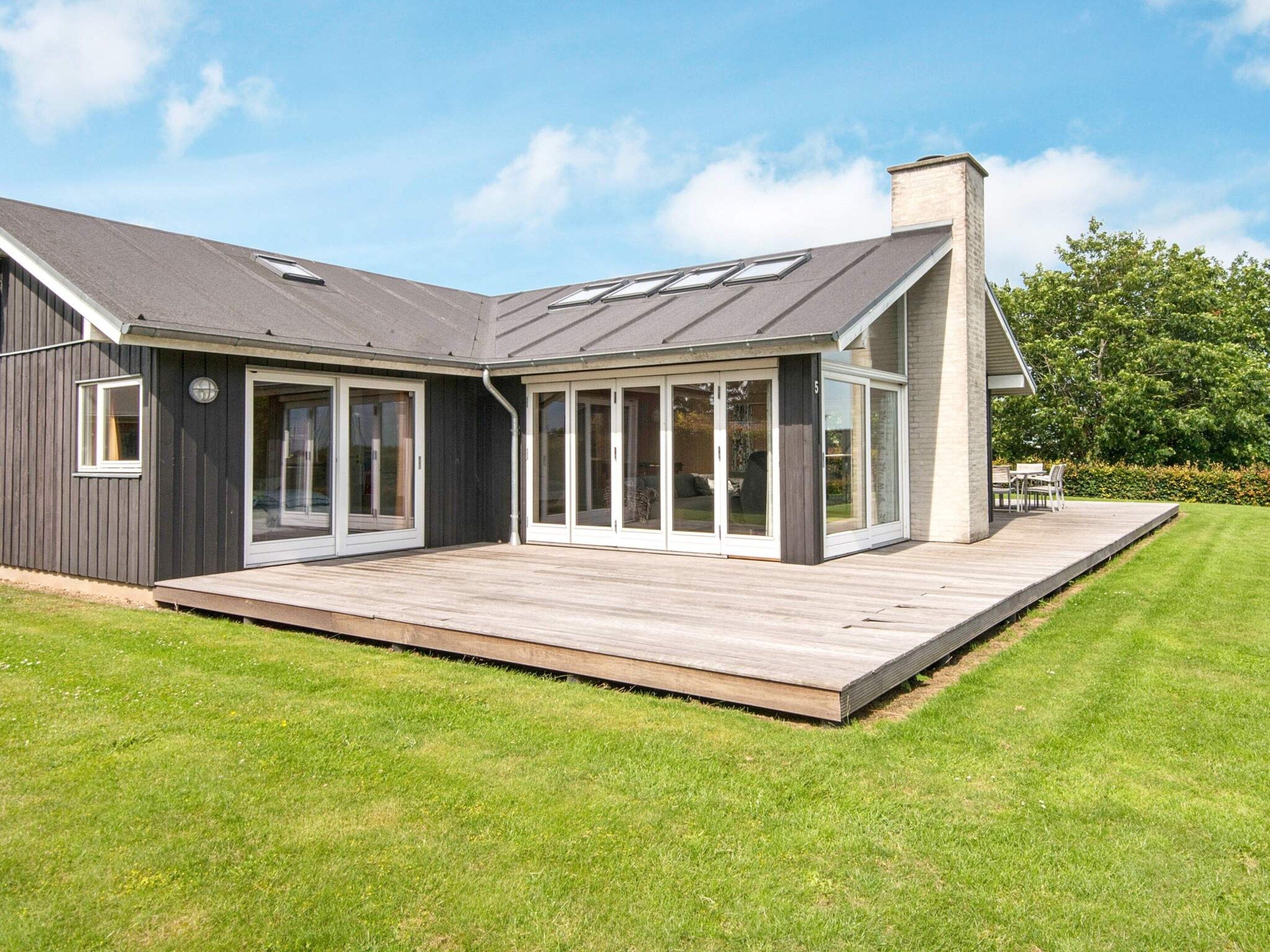 A modern house with a large deck, sliding glass doors, and a chimney.
