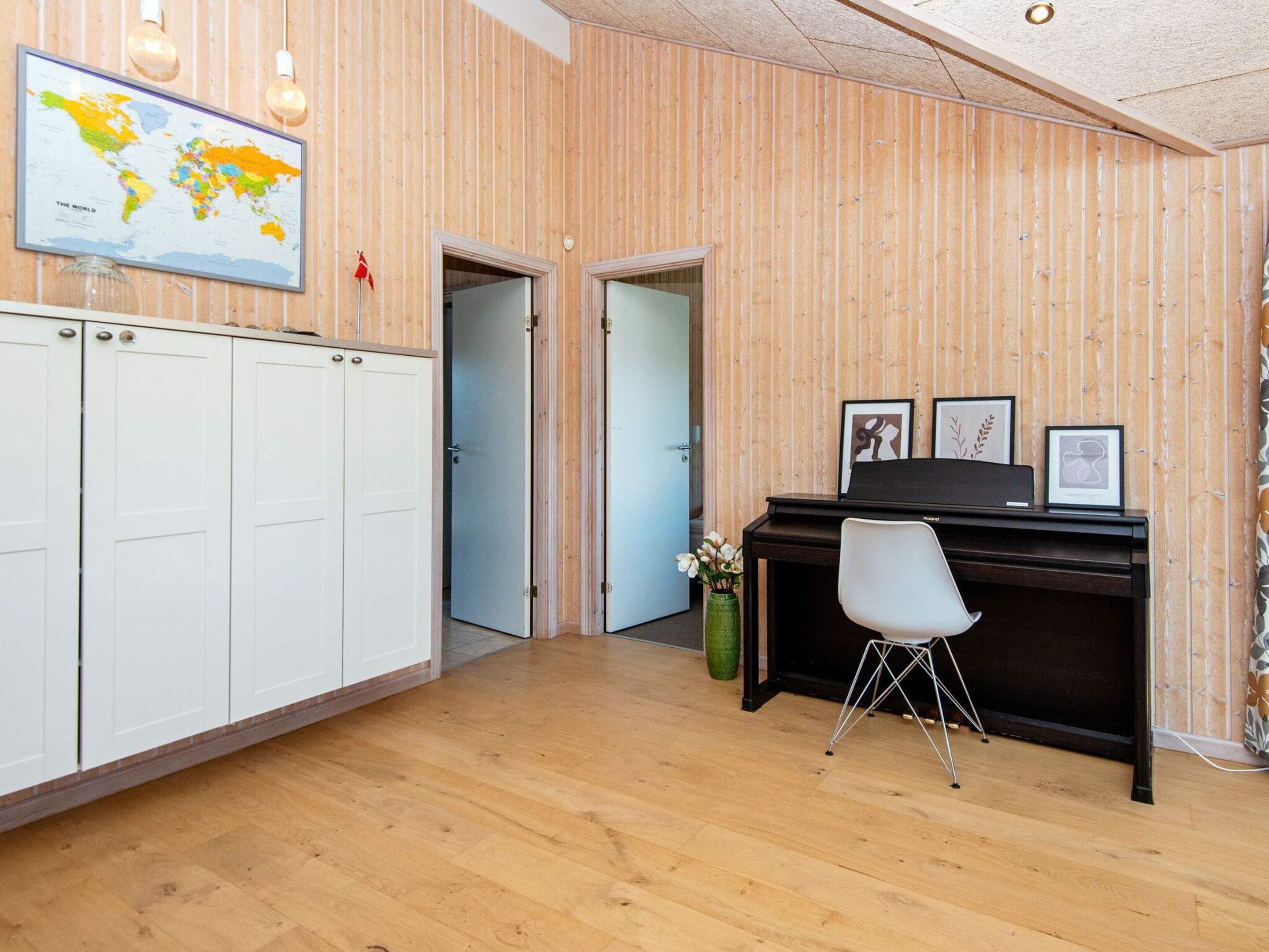 Une pièce avec un mur en bois, une armoire blanche, un bureau avec une chaise, une carte du monde accrochée au mur et des tableaux encadrés.
