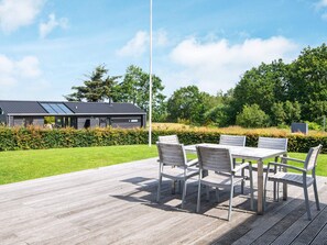 An outdoor patio with a table and chairs, a building with solar panels, and a hedge in the background. - 4 Star Holiday Home in Juelsminde (Horsens)