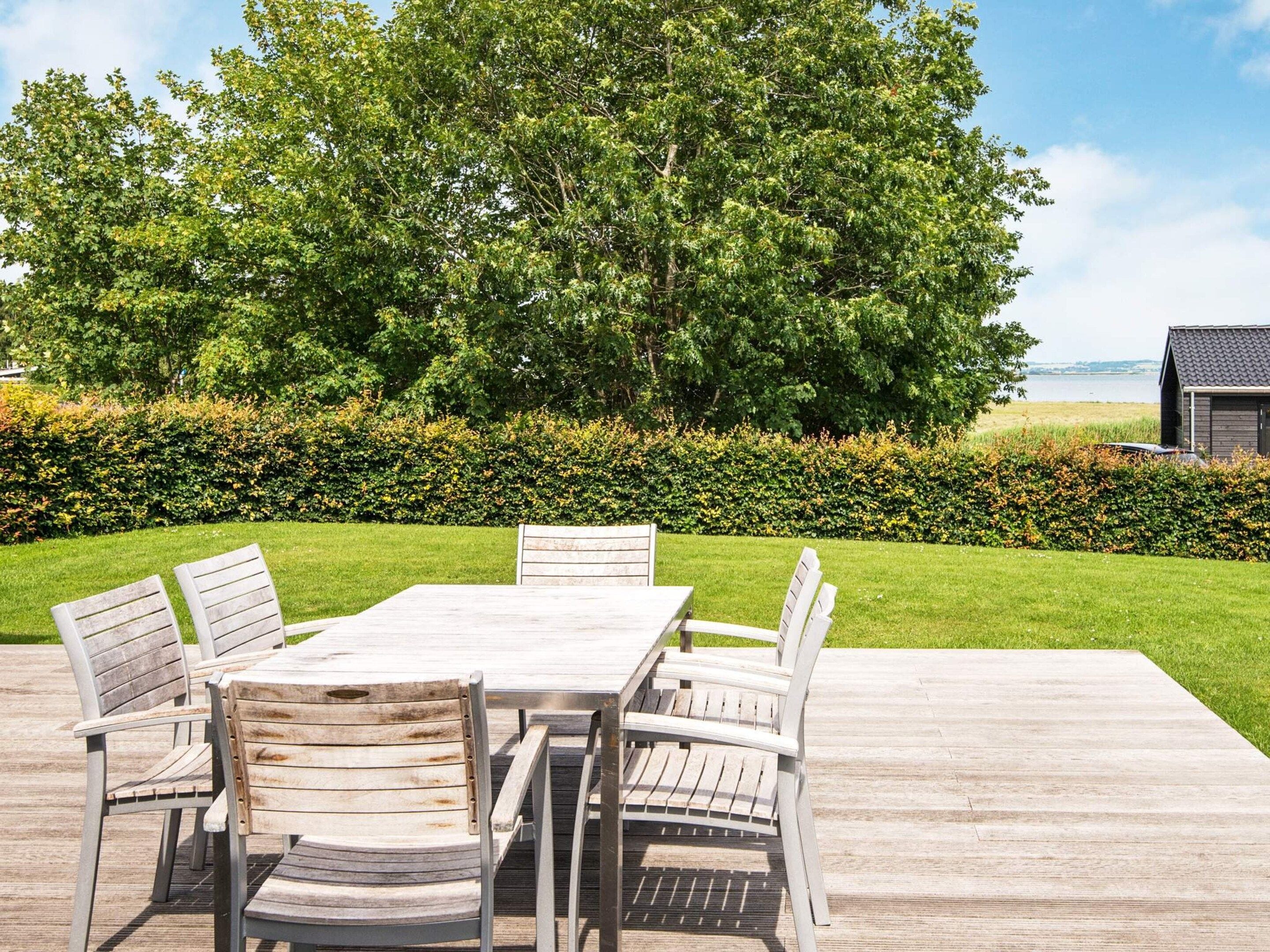 An outdoor patio with a wooden table and chairs, surrounded by a well-maintained lawn and a hedge.