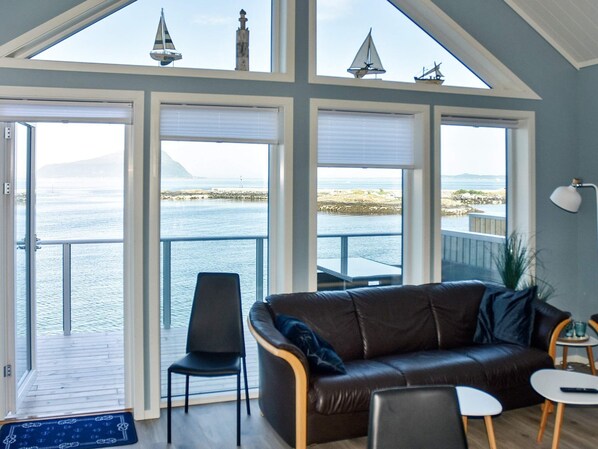 A room with a large window overlooking a body of water, a leather sofa, a small table, and a chair. - Holiday Home in BrattvÃ¥g (Ålesund)