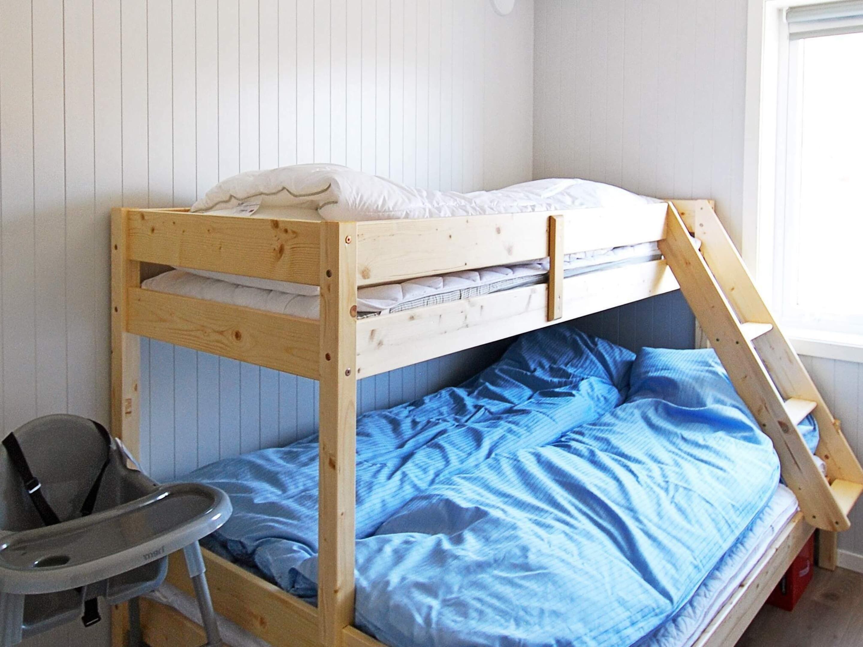 Ein Stockbett mit Holzbalken, einer blauen Matratze und einem weißen Kopfkissen.