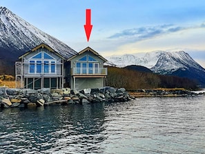 Eine Hütte mit Garage, gelegen an einem See vor einer Bergkulisse.