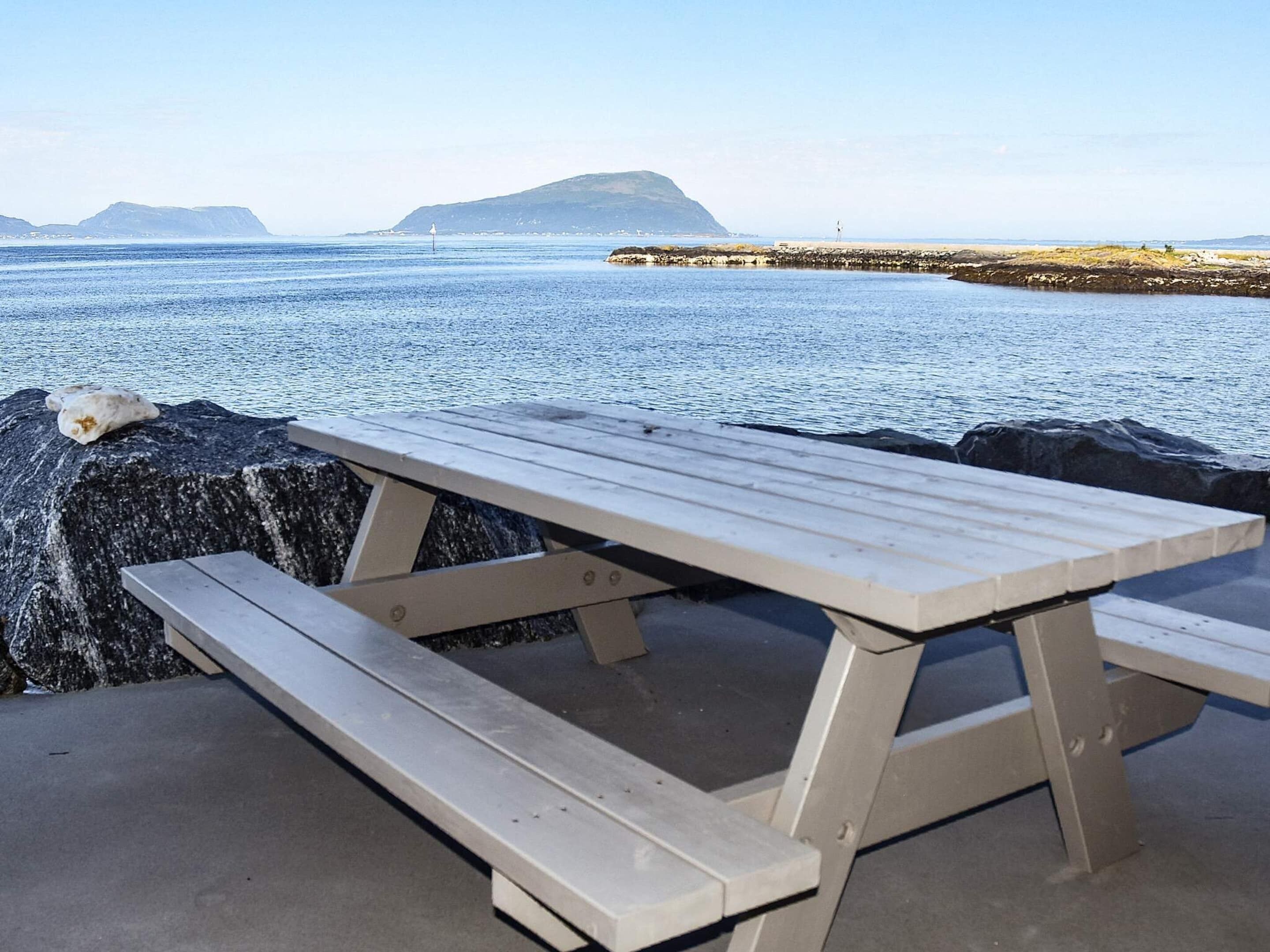 A picnic table by the water with a rocky shore and distant mountains.