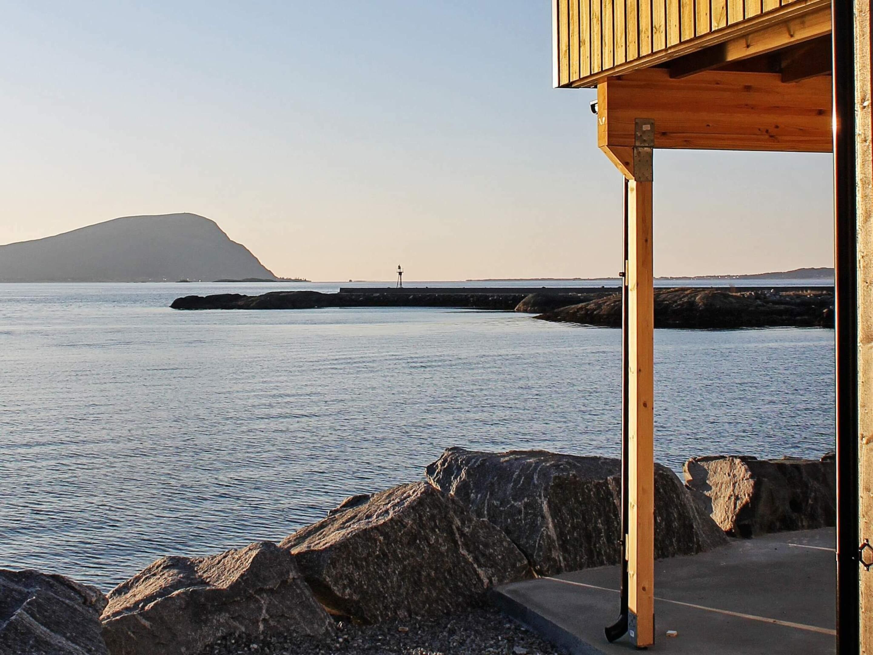 A coastal view with a wooden structure, a rocky shoreline, and a distant hill.
