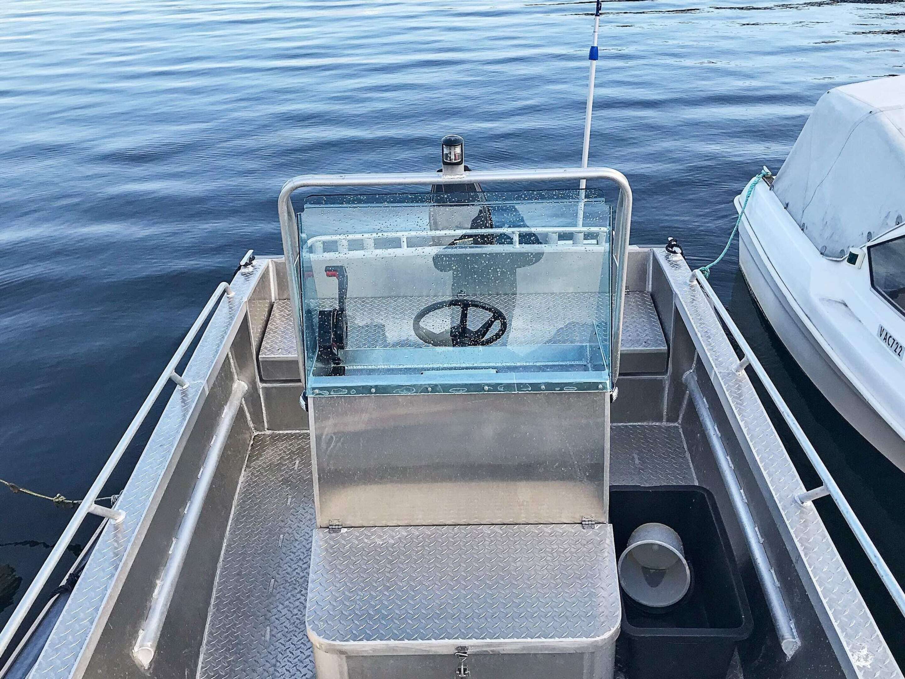 Interior de un bote con timón, baranda metálica y desagüe para agua.