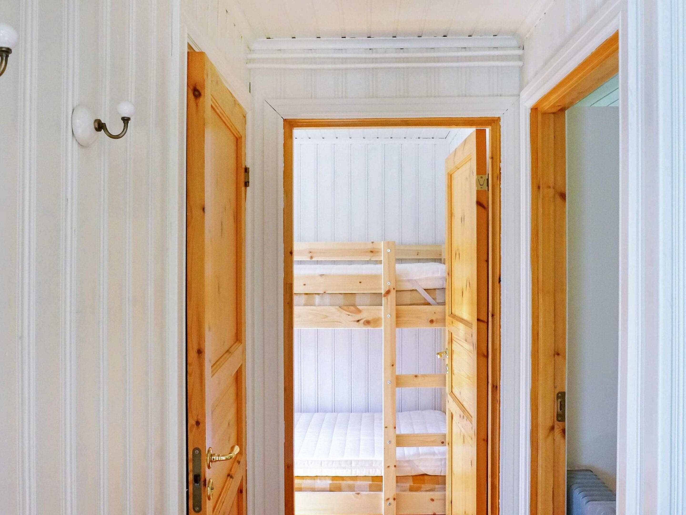 A narrow hallway with wooden doors leading to a room with bunk beds.