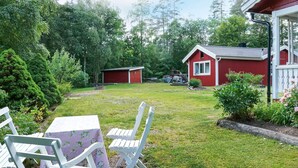 A red house with a white porch, a garden with a table and chairs, and a small shed in the background.