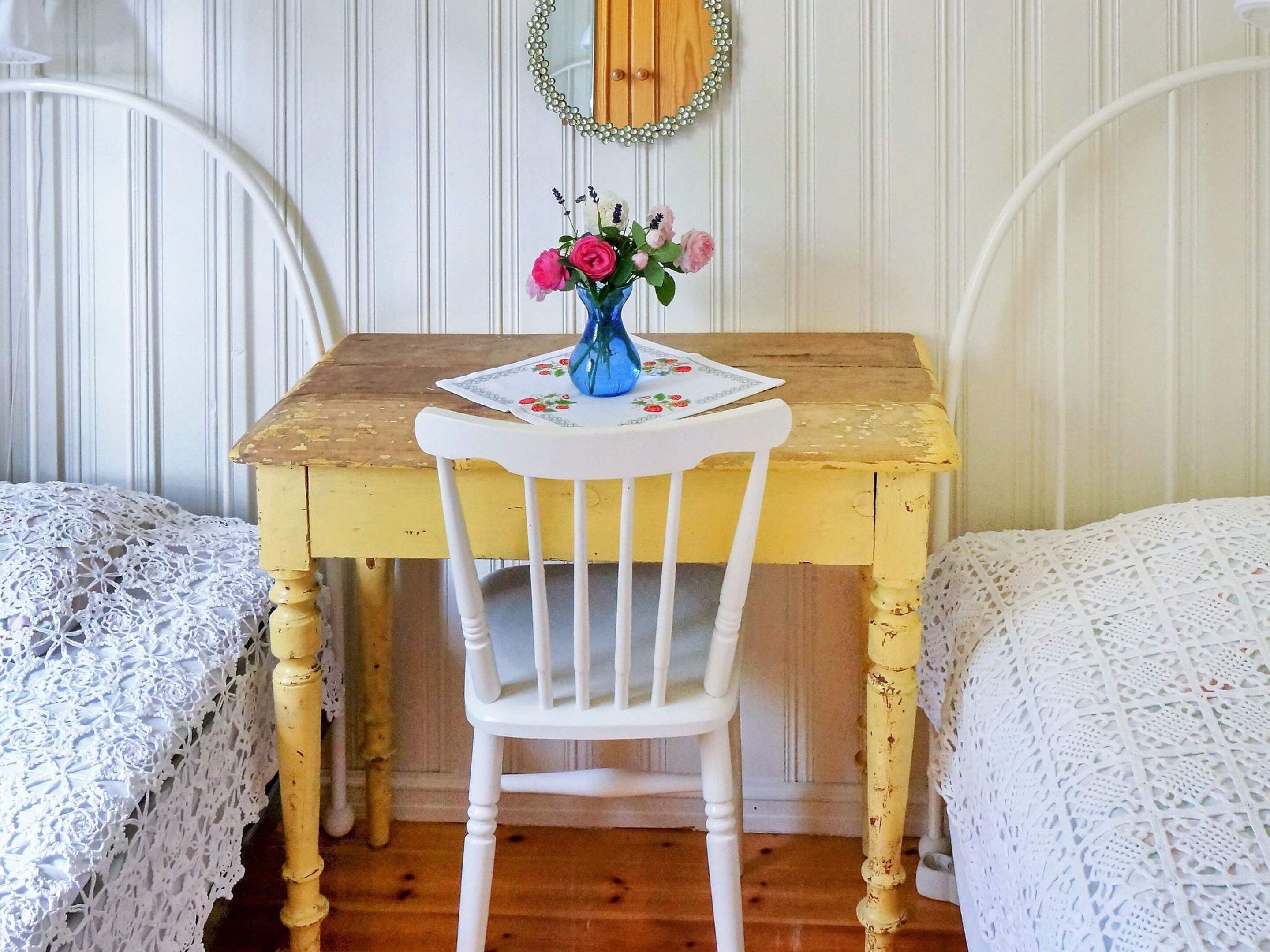Una habitación con una mesa de madera, una silla blanca y un espejo con marco de perlas.