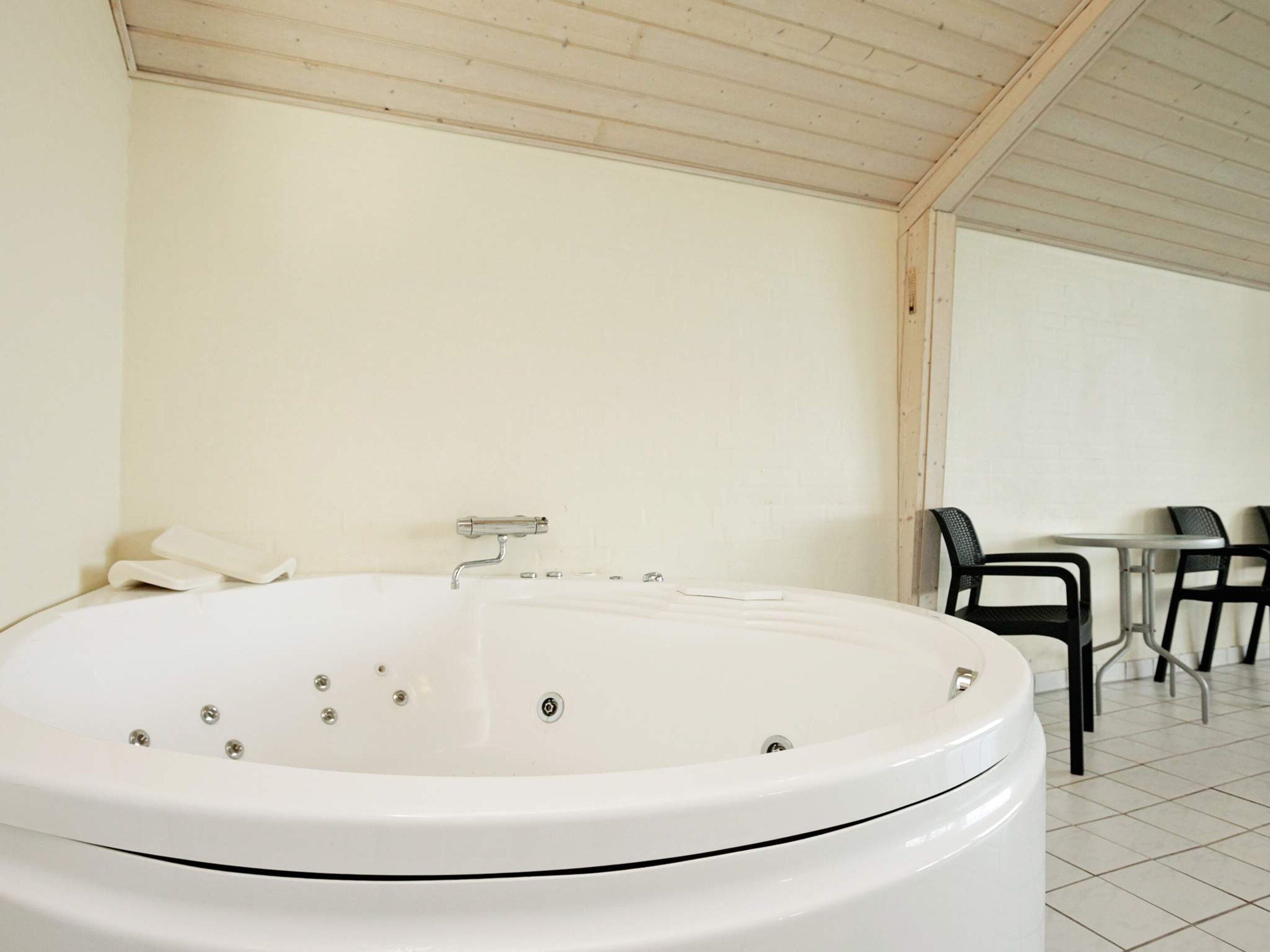 Ein modernes Badezimmer mit einer großen, weißen Badewanne, Holzboden und einer Sitzecke mit Stühlen und einem Tisch.