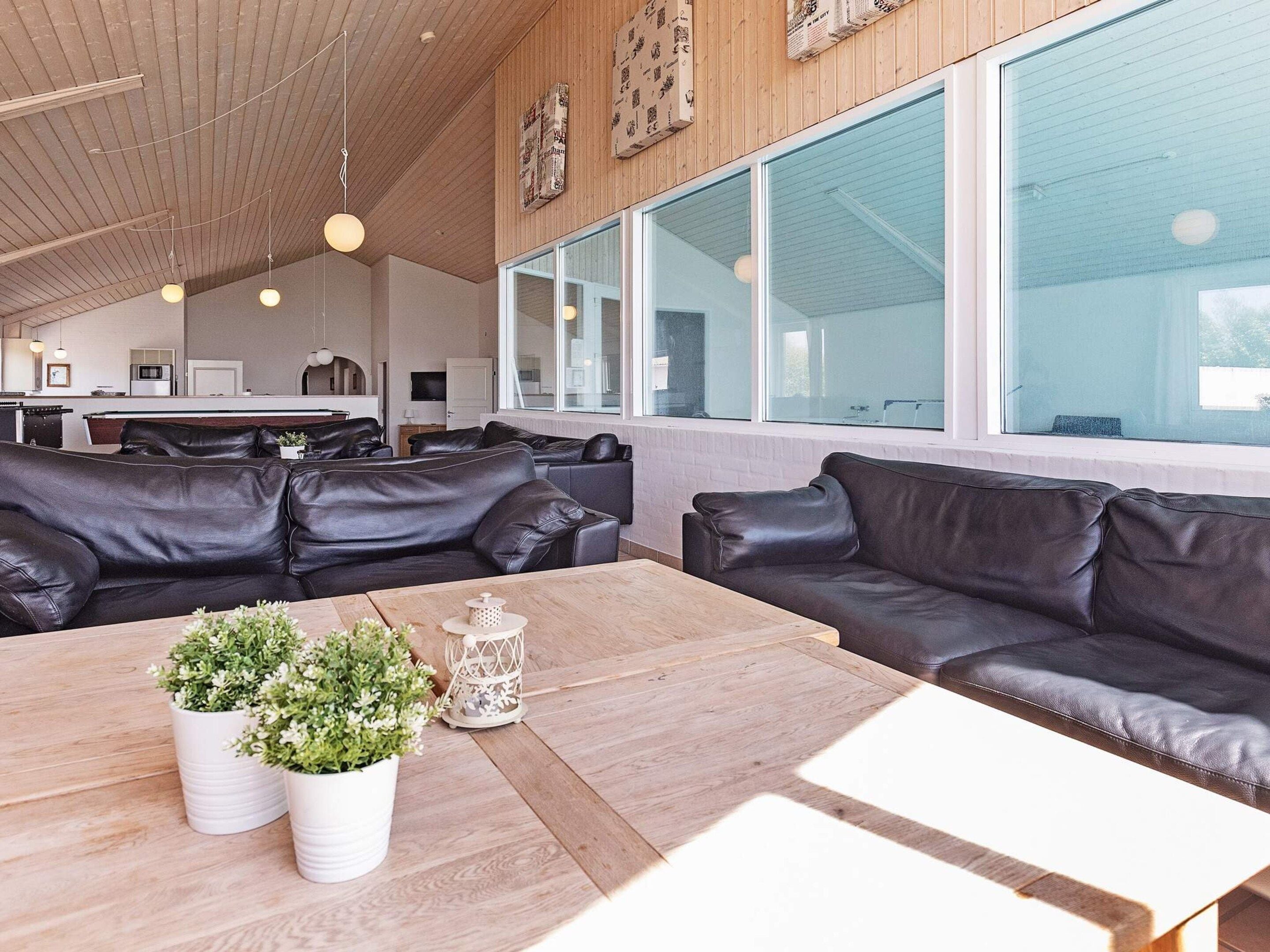 A modern interior with leather sofas, a wooden coffee table with plants, and large windows.