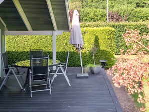 A covered outdoor seating area with a table and chairs, an umbrella, and a well-maintained hedge in the background. - 4 Star Holiday Home in Gorlev (Gørlev)