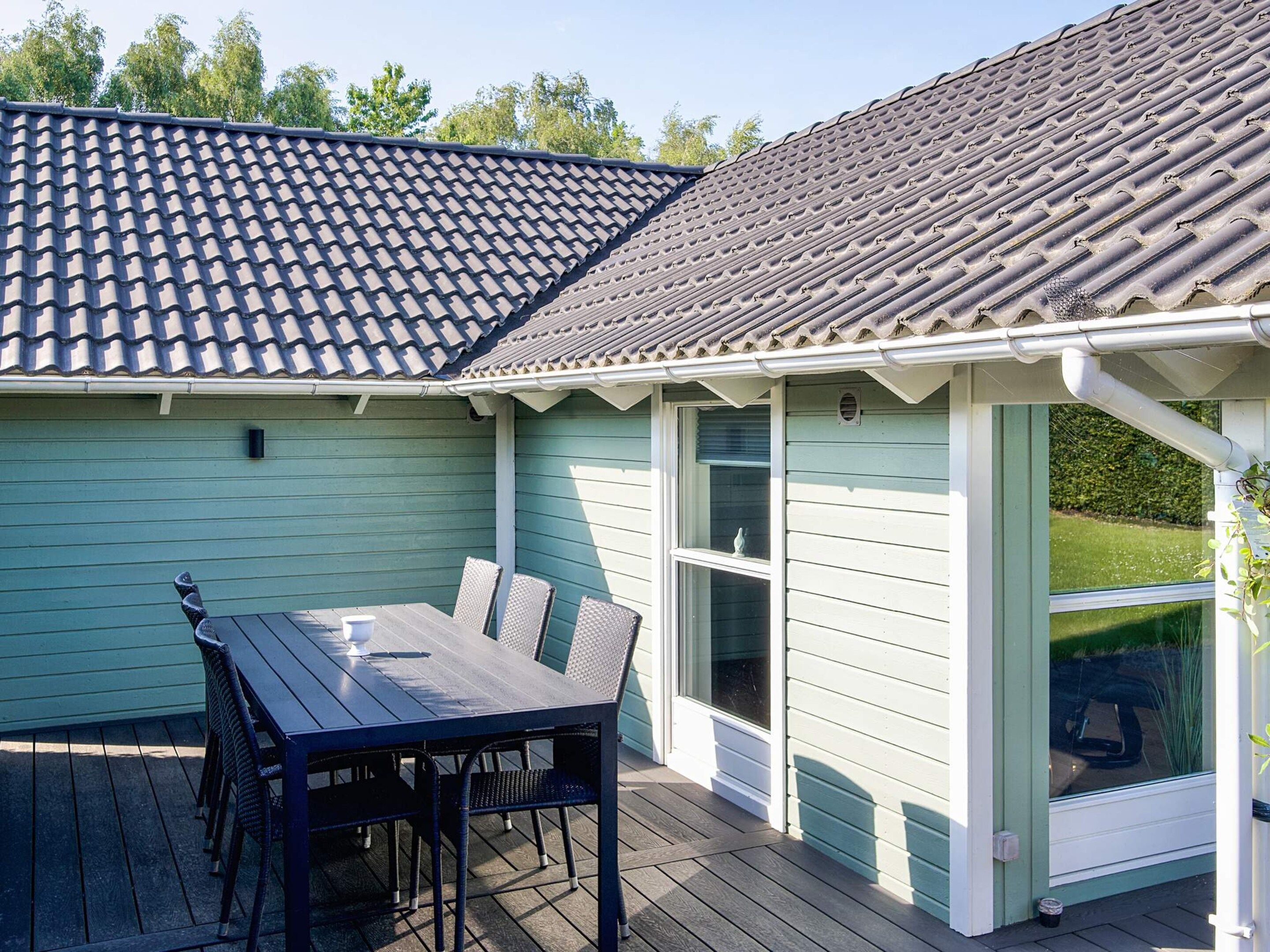 A covered patio with a table and chairs, a window, and a door leading to a green lawn.