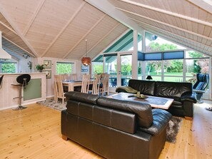 Un vaste espace de vie doté d’un haut plafond, d’un plancher en bois, d’un canapé en cuir, d’une table à manger avec des chaises et de grandes fenêtres offrant une vue sur l’extérieur.