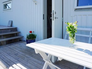 A white wooden table with a clear glass vase on a deck.