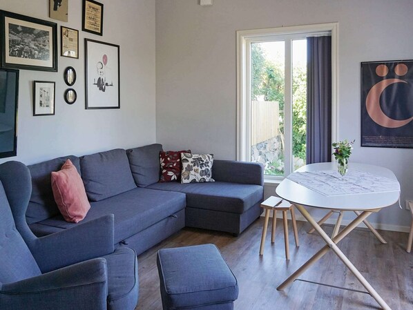 A modern living room with a grey sectional sofa, a small round table with a vase, and a large window with curtains.