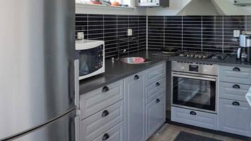 Une cuisine avec des meubles gris, un réfrigérateur en acier inoxydable, un four à micro-ondes, une cuisinière et un évier.