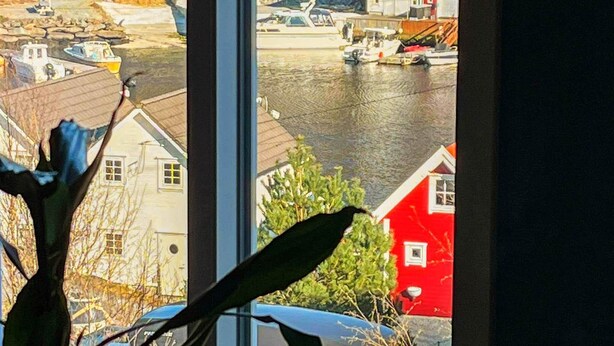 A view through a window of a coastal town with houses, boats, and a red building. - Holiday Home in Auklandshamn (Sveio)