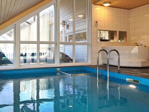 An indoor swimming pool with clear glass walls, a blue pool edge, and a white bathtub with a shower. - Holiday Home in Auklandshamn (Sveio)