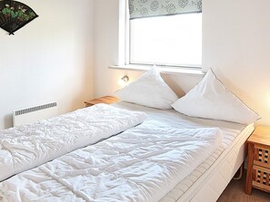 A bedroom with a bed, a bedside table, a nightstand, a window, and a wall-mounted fan.