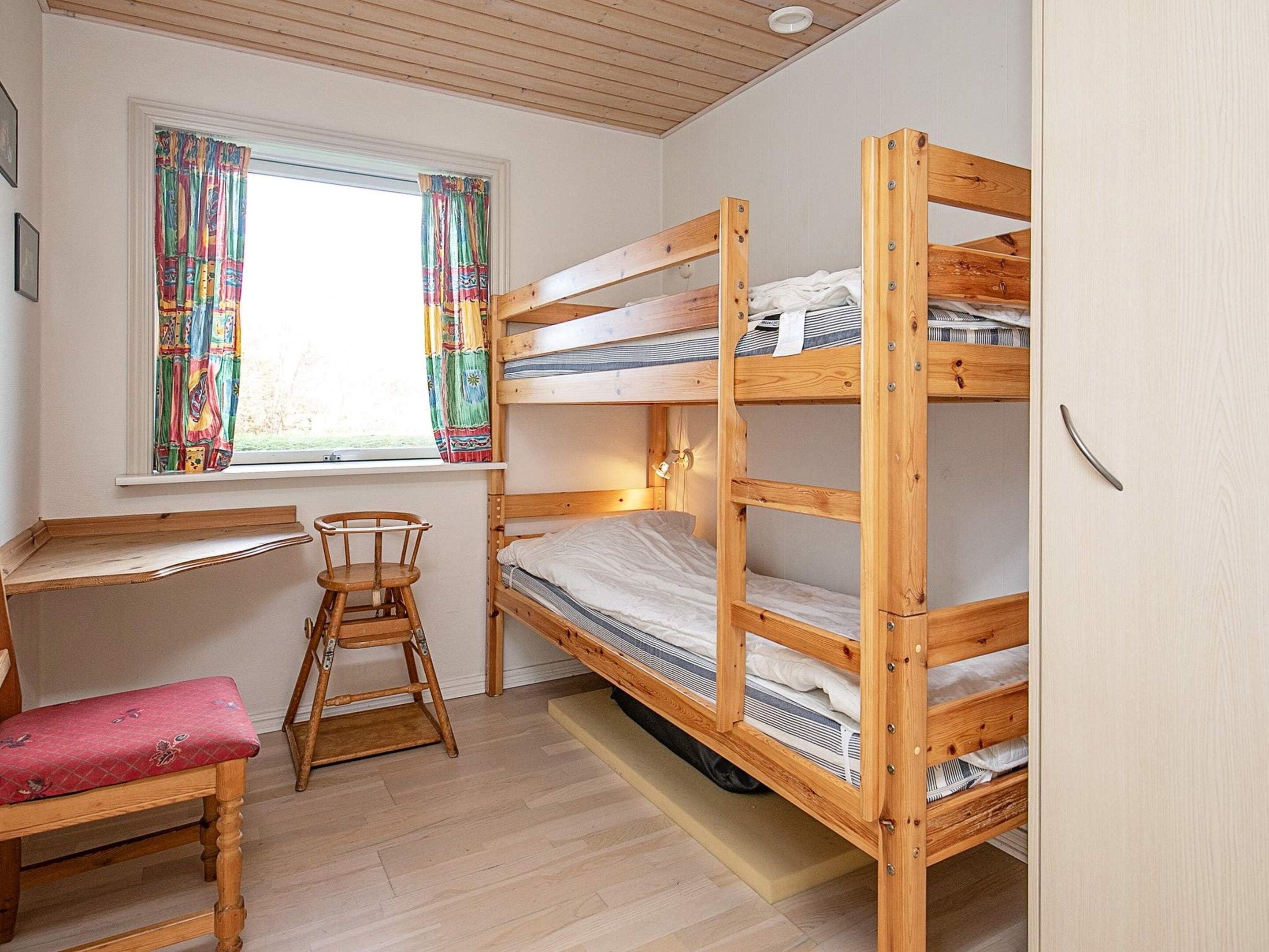 Habitación con literas, un escritorio, una silla, una ventana con cortinas de colores y piso de madera.