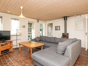A living room with a wooden ceiling, a grey sofa, a wooden coffee table, a television, and a fireplace.