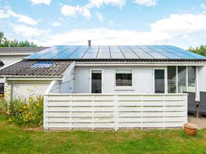 A house with a solar panel roof, a white fence, and a garden with yellow flowers.
