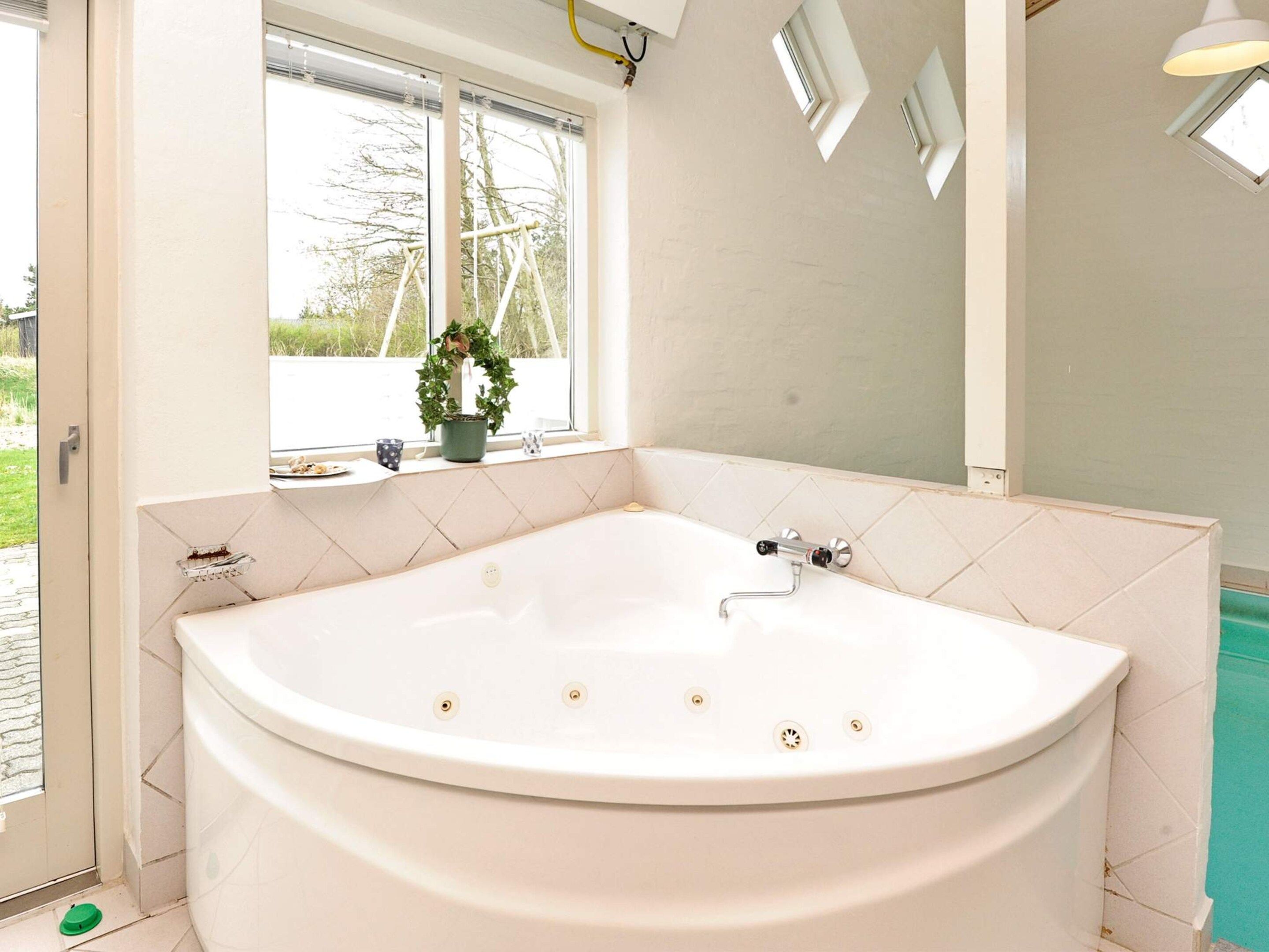 A bathroom with a freestanding bathtub, a window with a view of trees, and a potted plant on the windowsill.