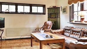 Uma sala de estar com piso de madeira, um sofá de couro marrom, uma mesa de centro de madeira, uma poltrona listrada e um armário verde.