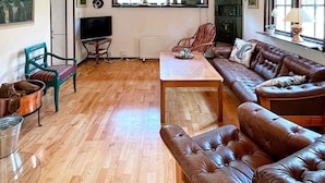 Uma sala de estar com piso de madeira, um sofá de couro marrom, uma mesa de centro de madeira e uma televisão.