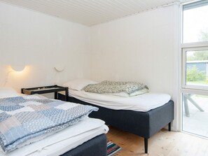 A bedroom with two beds, a nightstand, a wall-mounted lamp, and a large window. - 4 Star Holiday Home in Ebeltoft (Ebeltoft)