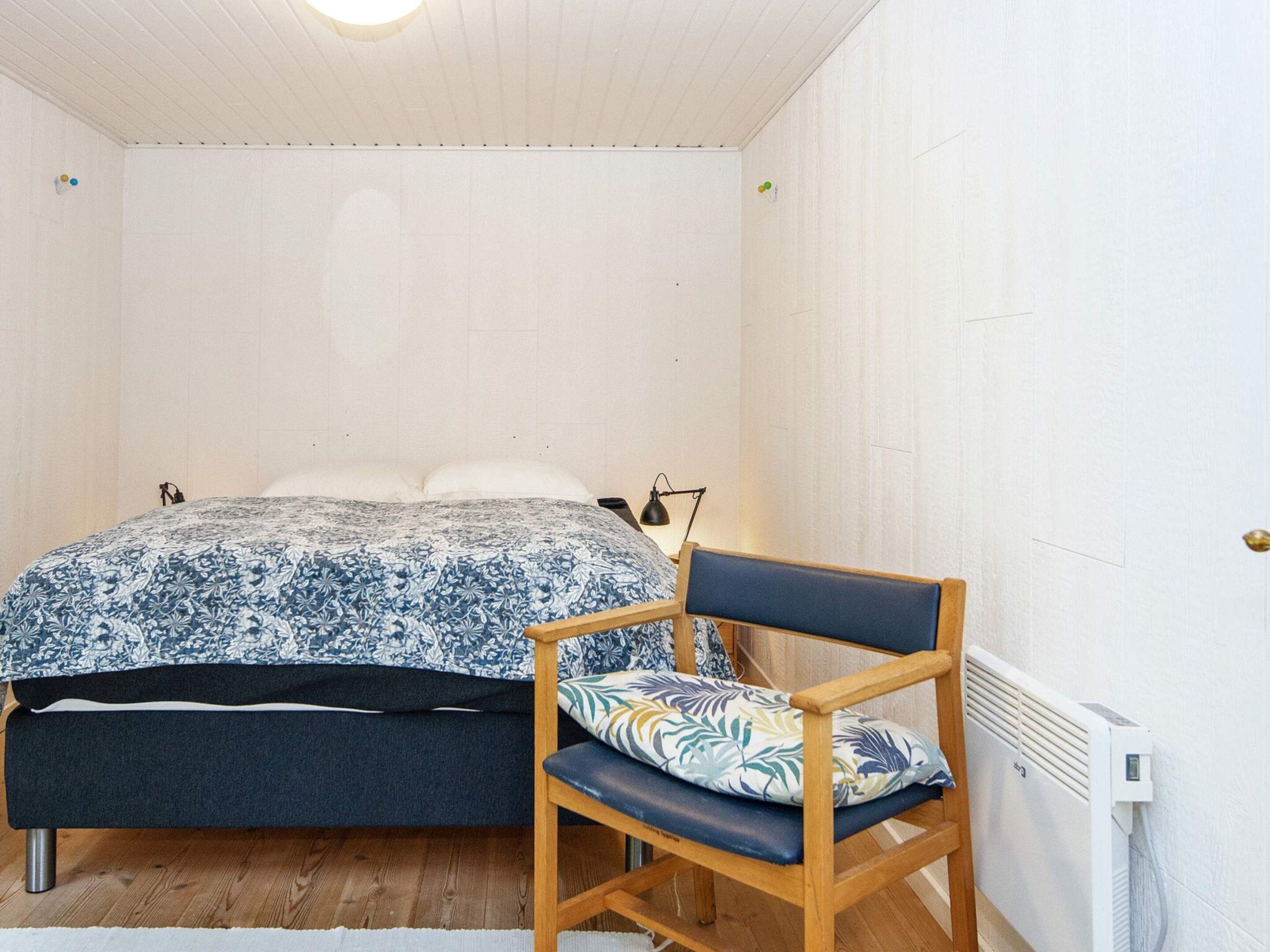 A bedroom with a bed, a chair, a bedside table, and a radiator.