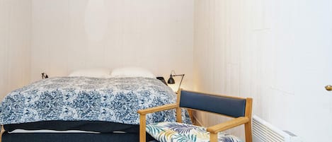 A bedroom with a bed, a chair, a bedside table, and a radiator.