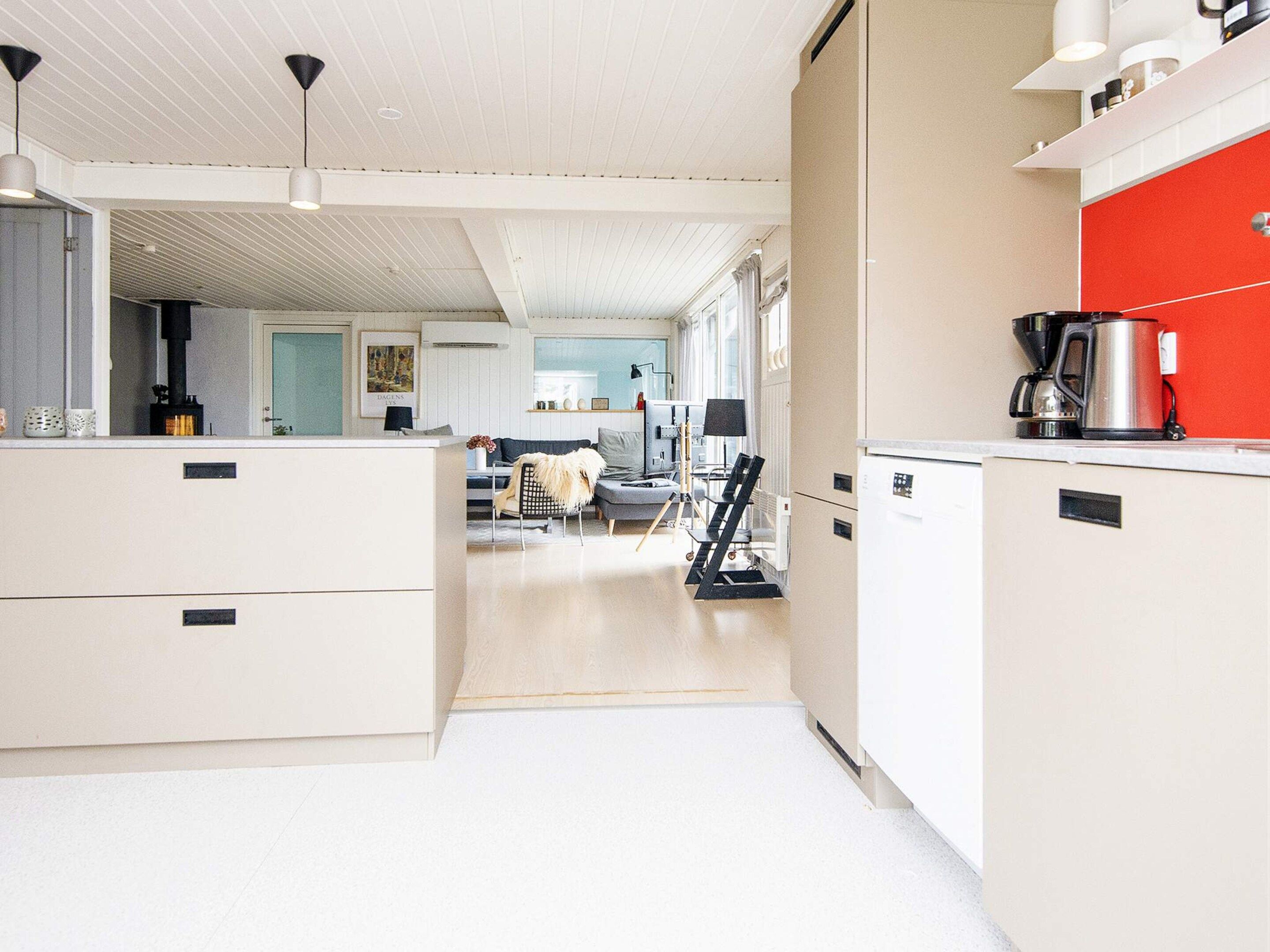 A modern kitchen with white cabinetry, a red accent wall, and a coffee machine.